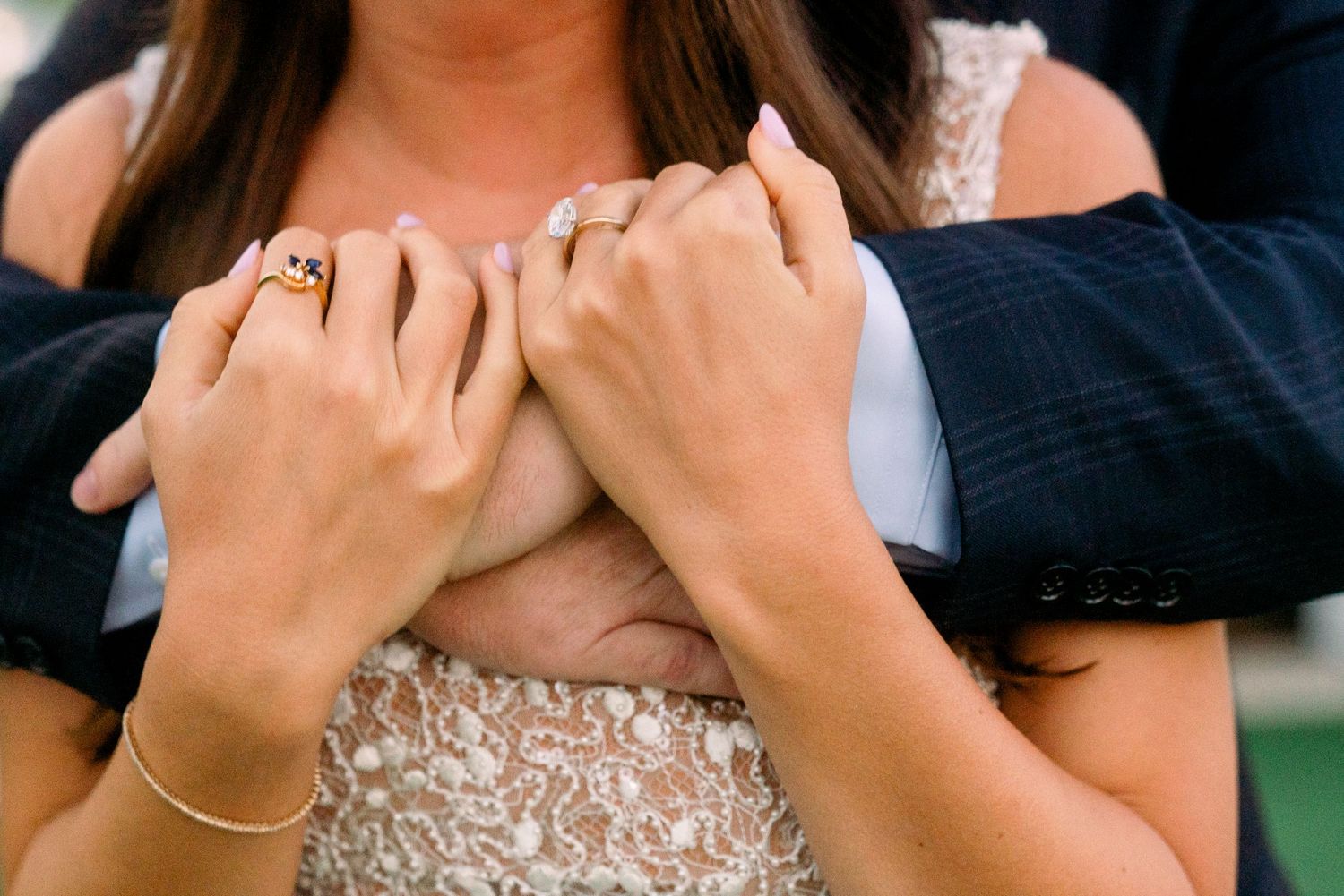 Close-up of hands with rings and jewelry embracing in formal wear.