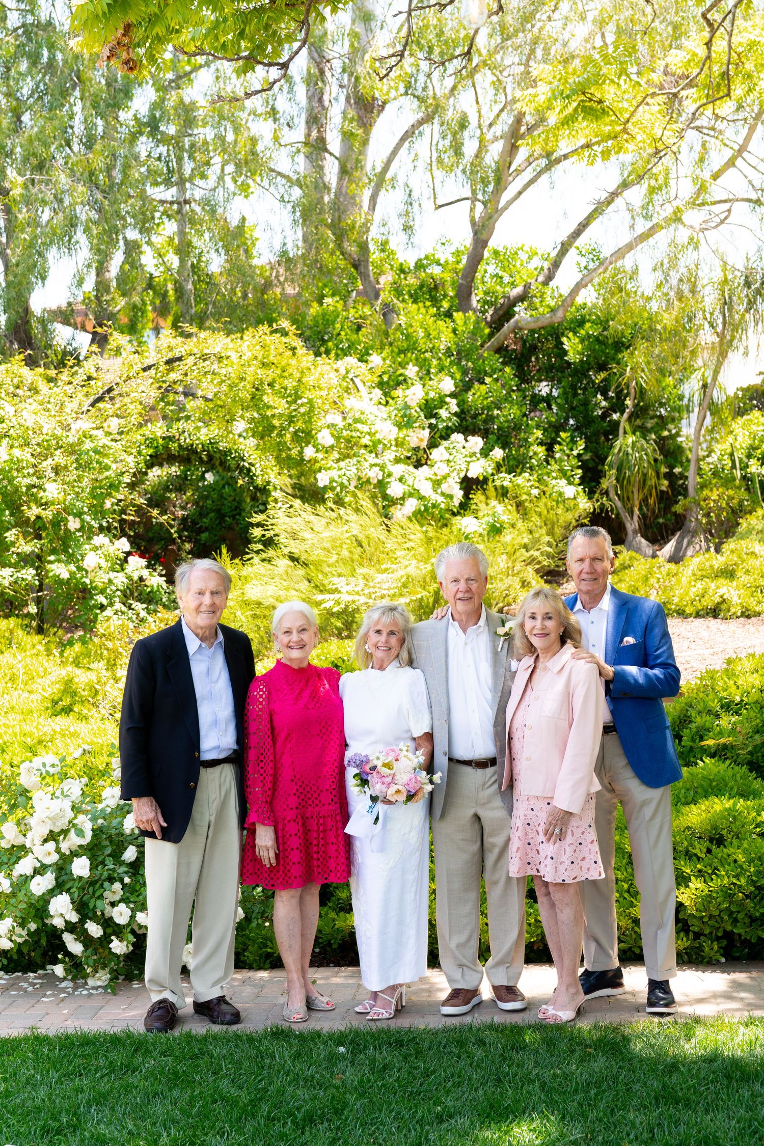A group gathers for a photo in a lush garden setting with blooming flowers and greenery in the background.