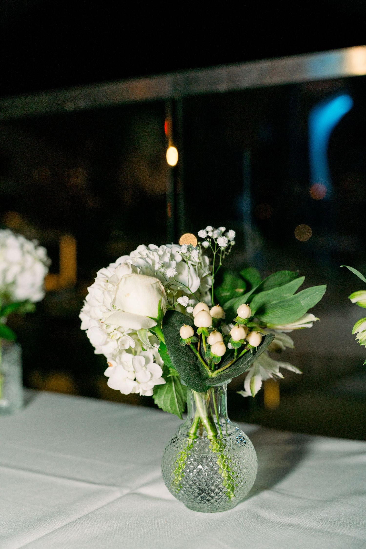 White floral centerpiece arrangement in a cut glass vase on a table with ambient lighting.
