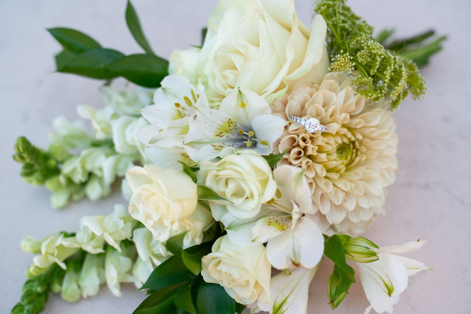 Elegant white wedding bouquet featuring roses, dahlias, and green accents against a light background.
