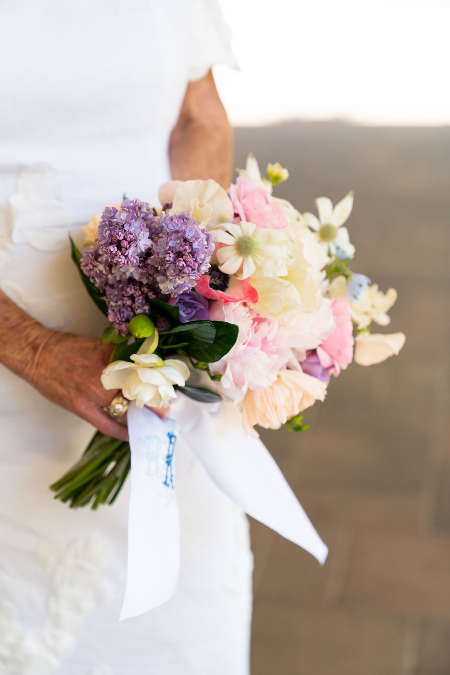 A delicate wedding bouquet with purple lilacs, pink roses, and white flowers wrapped in ribbon.