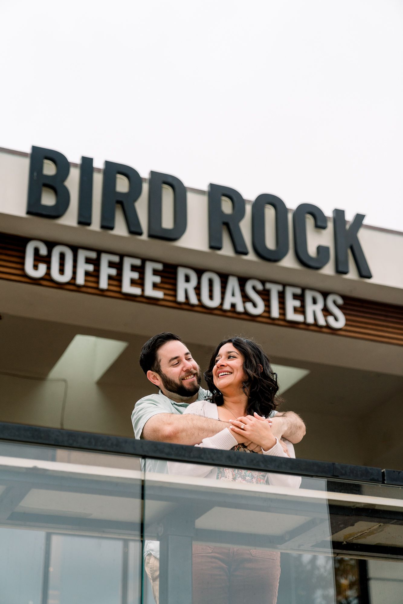 Happy couple embracing outside Bird Rock Coffee Roasters storefront.