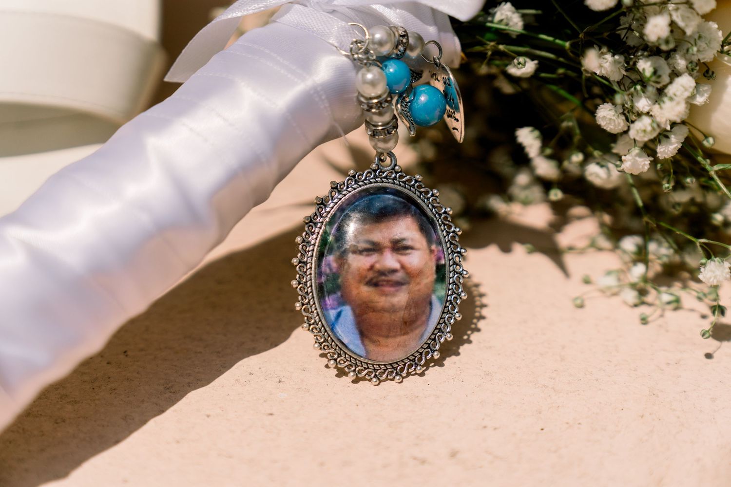 Wedding bouquet with a decorative silver pendant charm featuring a photograph, adorned with blue crystal accents.