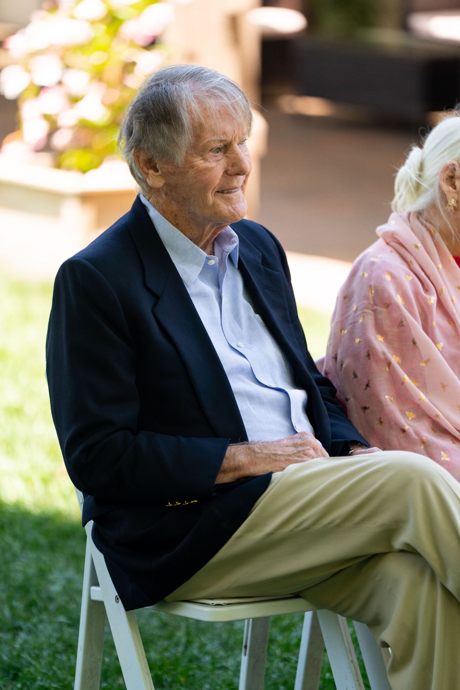 Two guests seated outdoors at an event on white folding chairs.