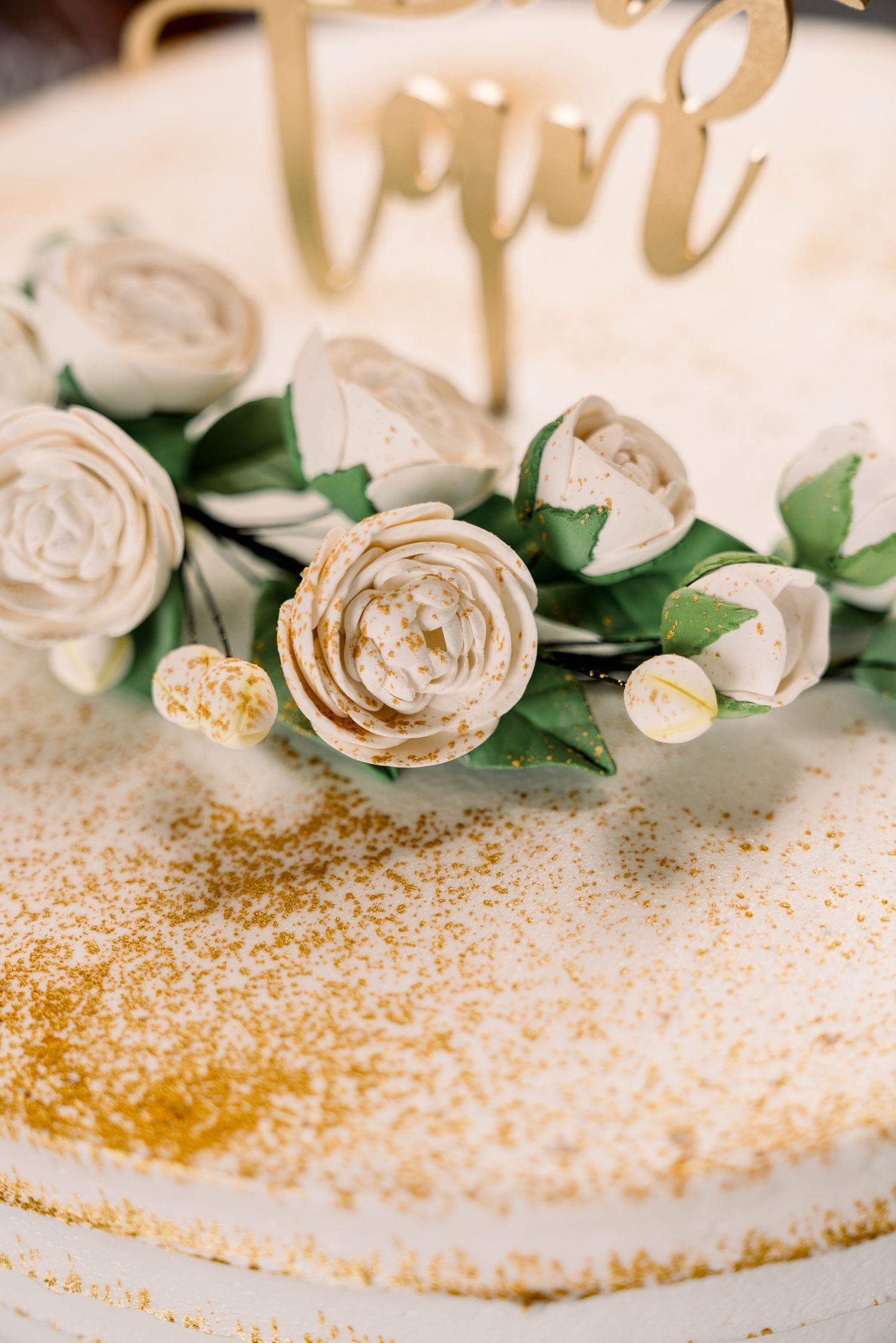 Close up of white roses and gold glitter detail on an elegant wedding cake.