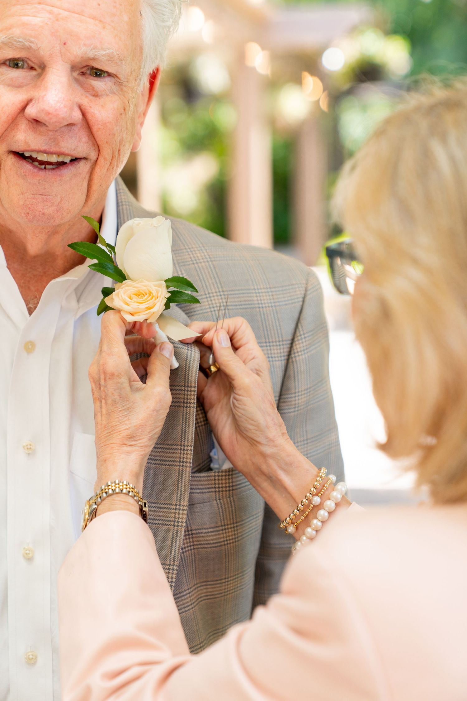 A touching moment as a yellow rose boutonniere is being pinned onto a light grey suit jacket.