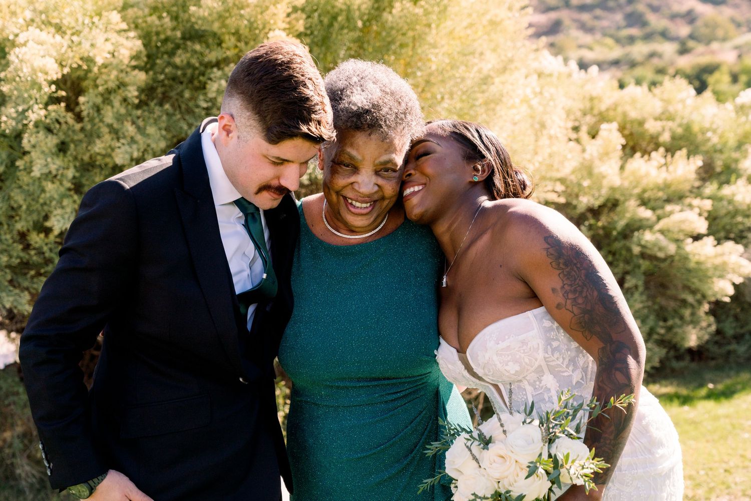 Joyful embrace shared between three wedding attendees during outdoor celebration.