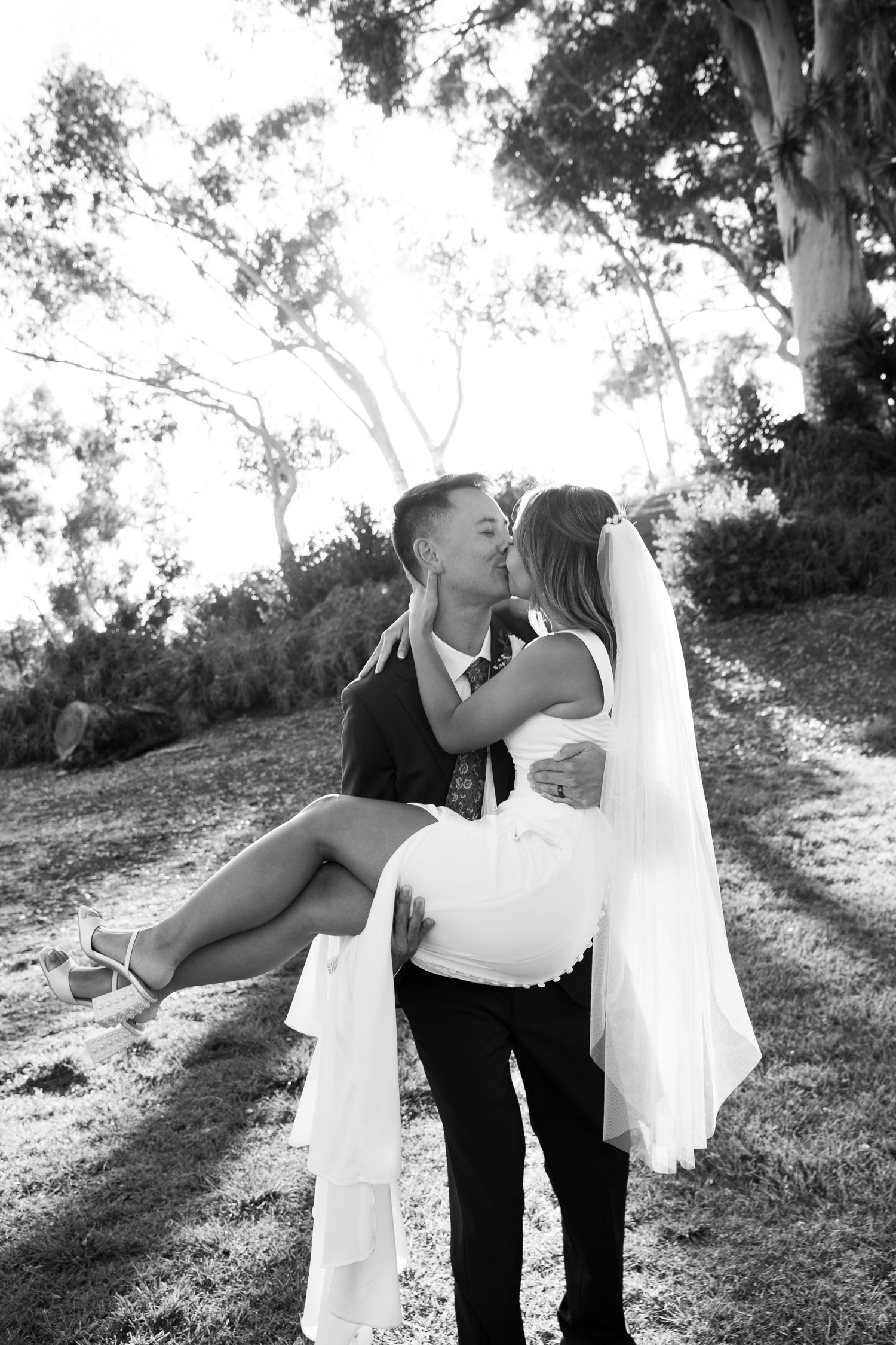 A black and white wedding photo captures a romantic lift pose outdoors.