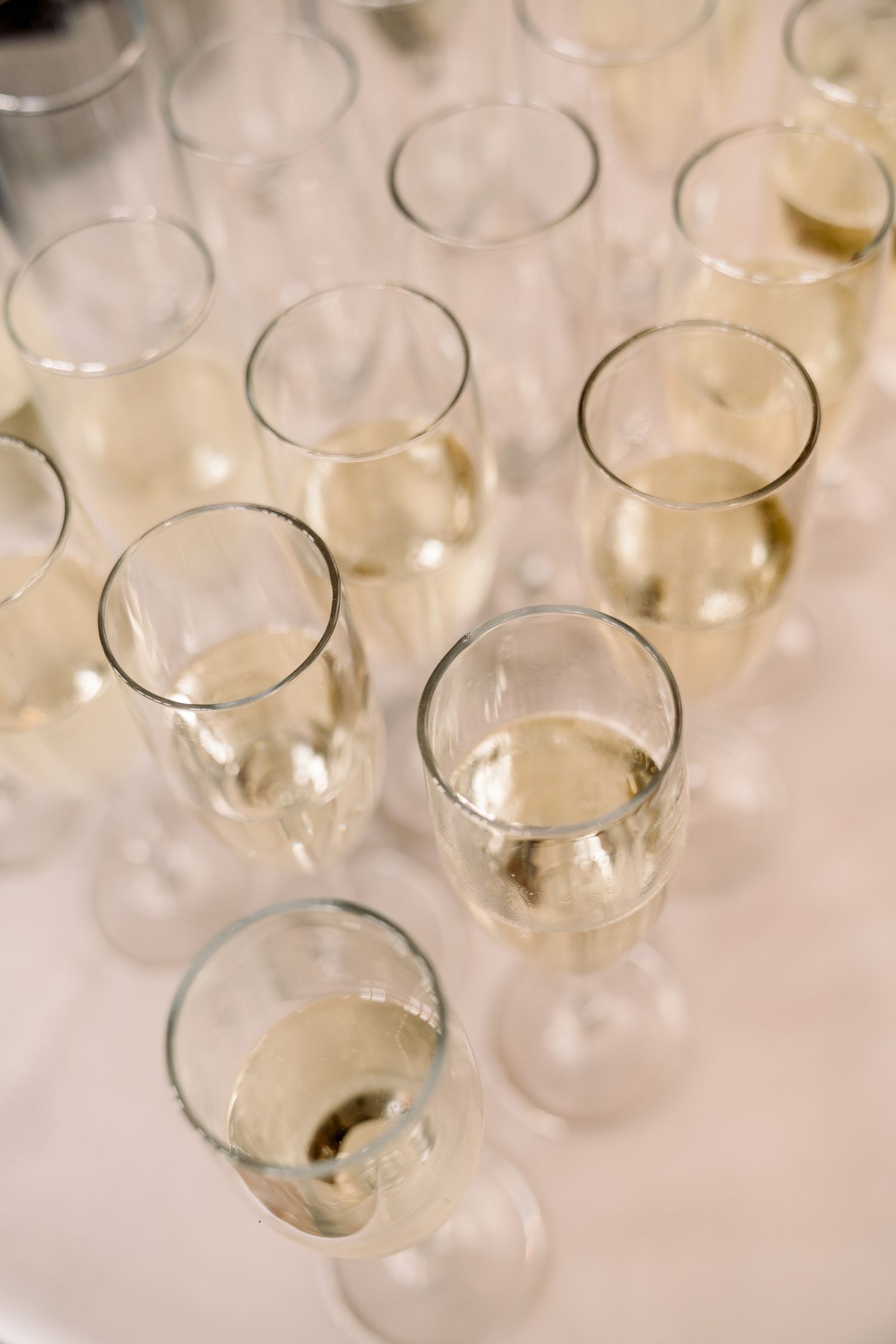 Multiple champagne flutes filled with sparkling wine arranged on a white tablecloth.