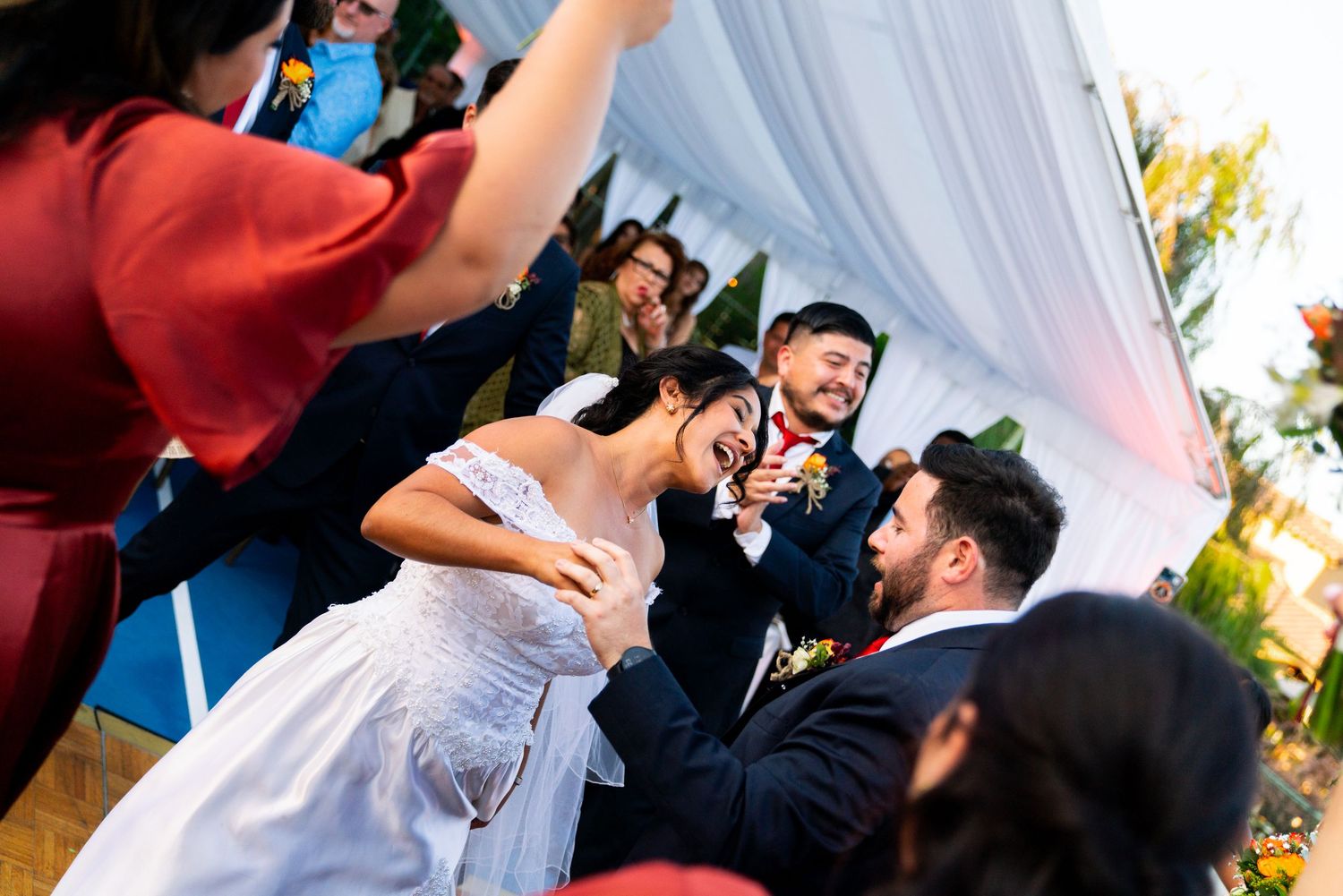 A candid moment between people dancing and celebrating at an outdoor wedding reception under white draping.