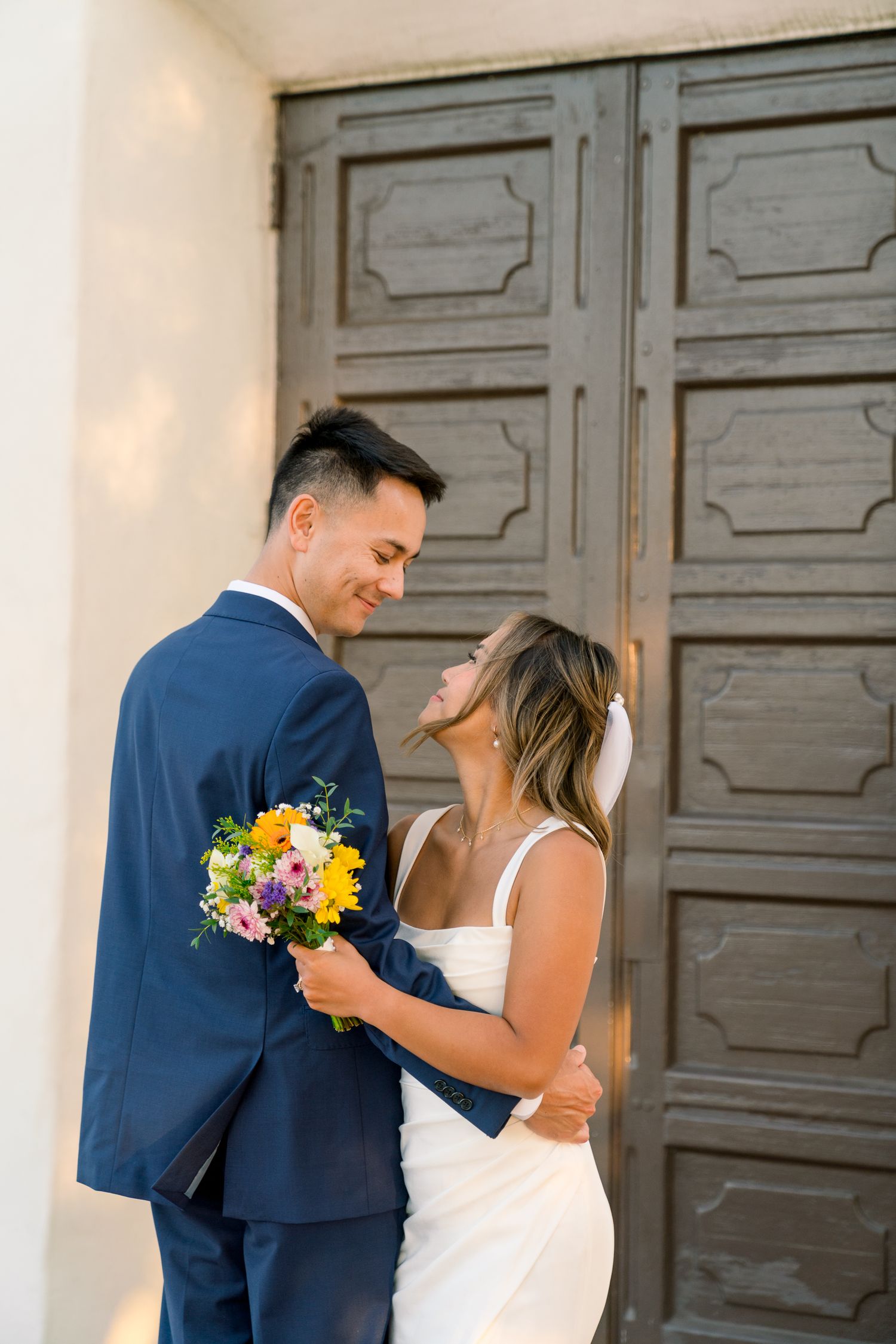 A tender moment shared between a couple holding a colorful bouquet against an ornate vintage door.