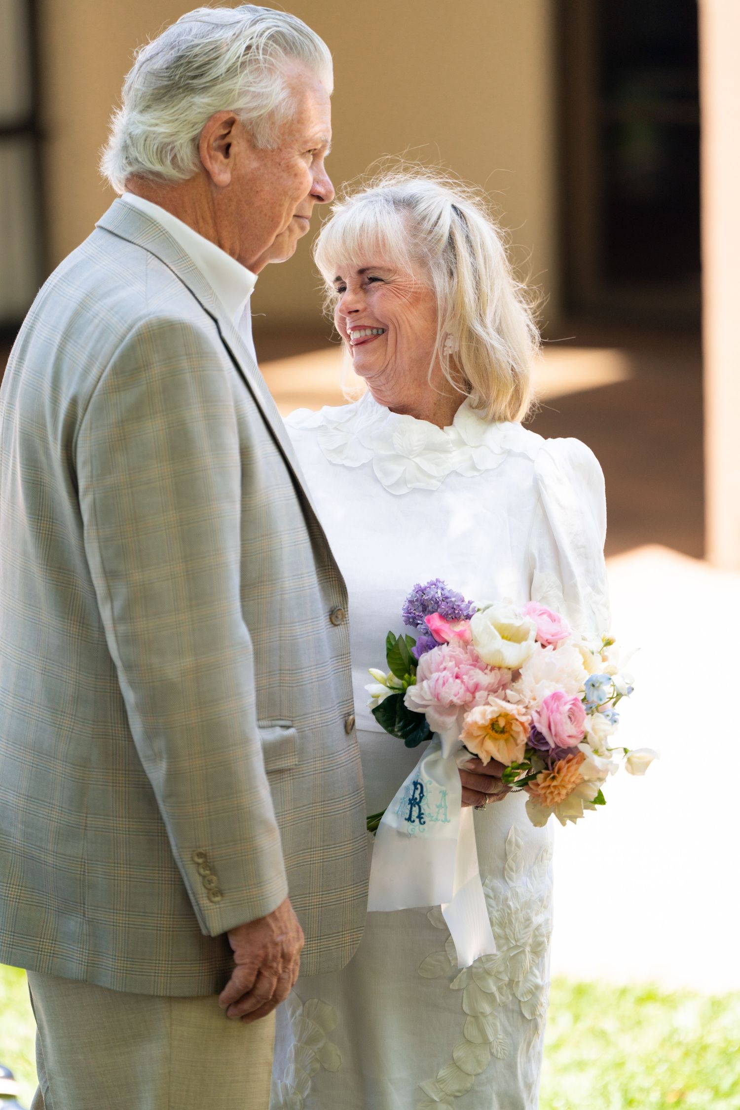 Senior couple shares a joyful moment at their wedding ceremony with a beautiful pastel and purple bouquet.