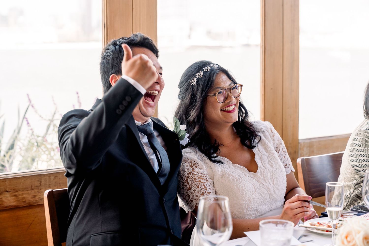 Happy couple reacting with joy during wedding reception toast.