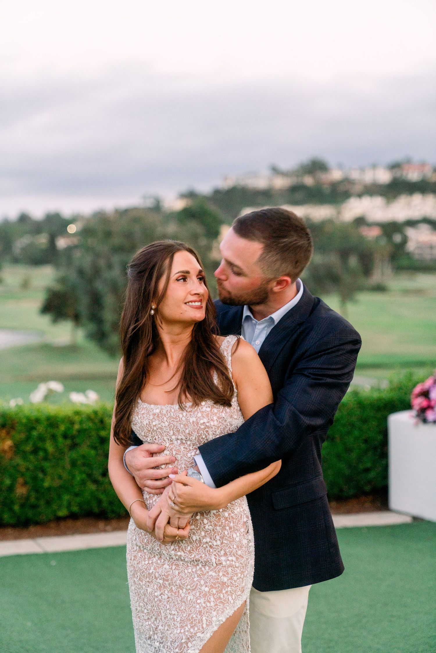 Romantic moment between couple in formal attire on an outdoor terrace overlooking a golf course.