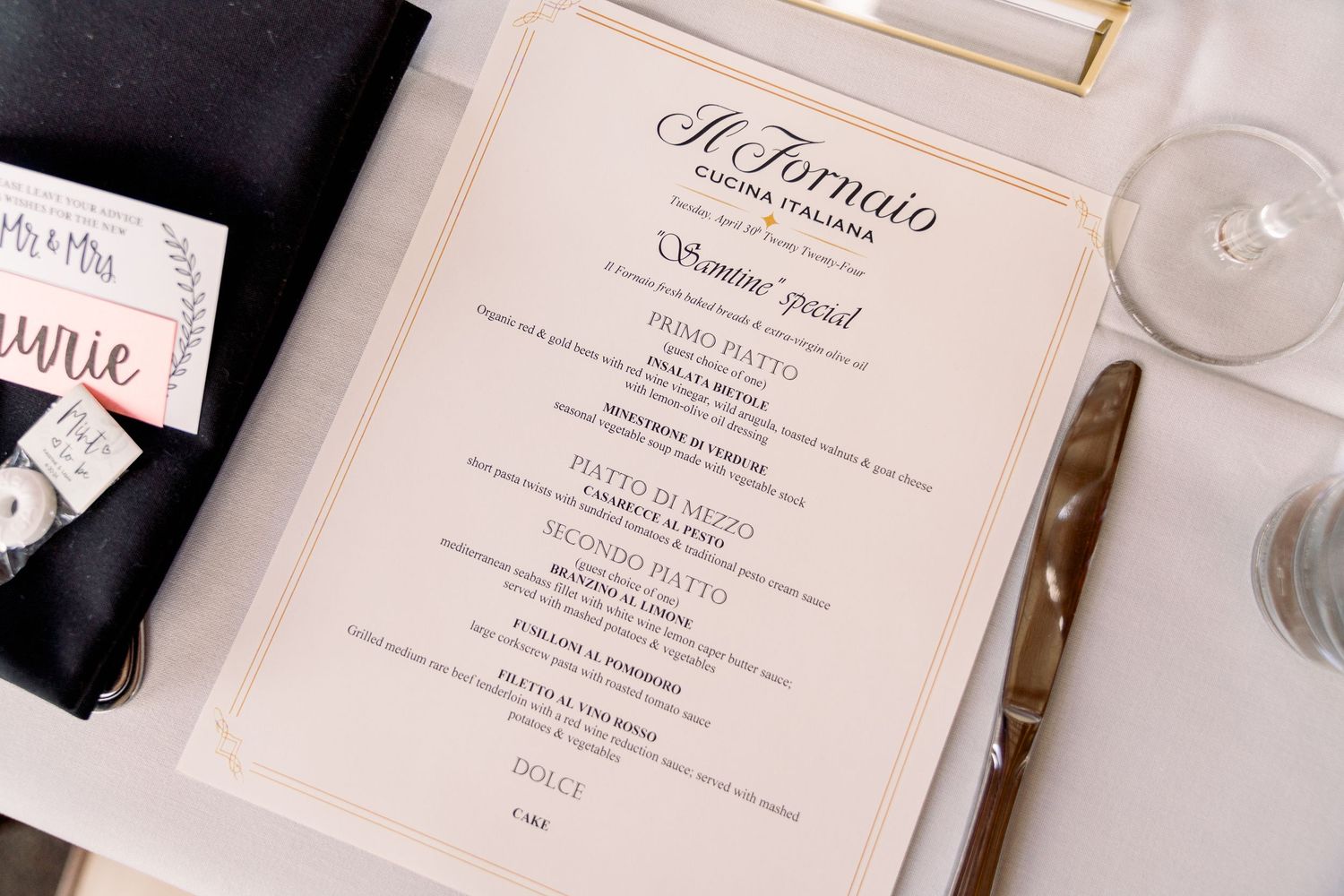 An elegant wedding menu card with 'Il Tartufo' text laid on a white table next to a black napkin and drinking glass.