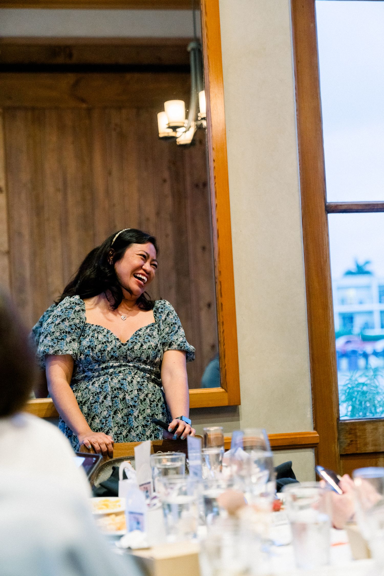 A guest in a floral dress laughs joyfully at a wedding reception.