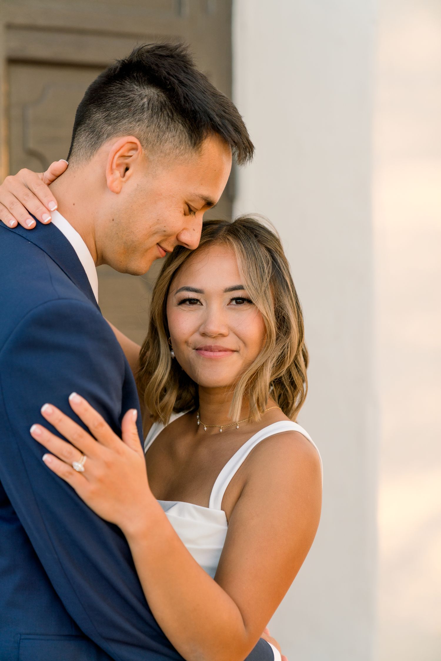A couple shares an intimate moment during their wedding shoot, with the bride in white and groom in navy.