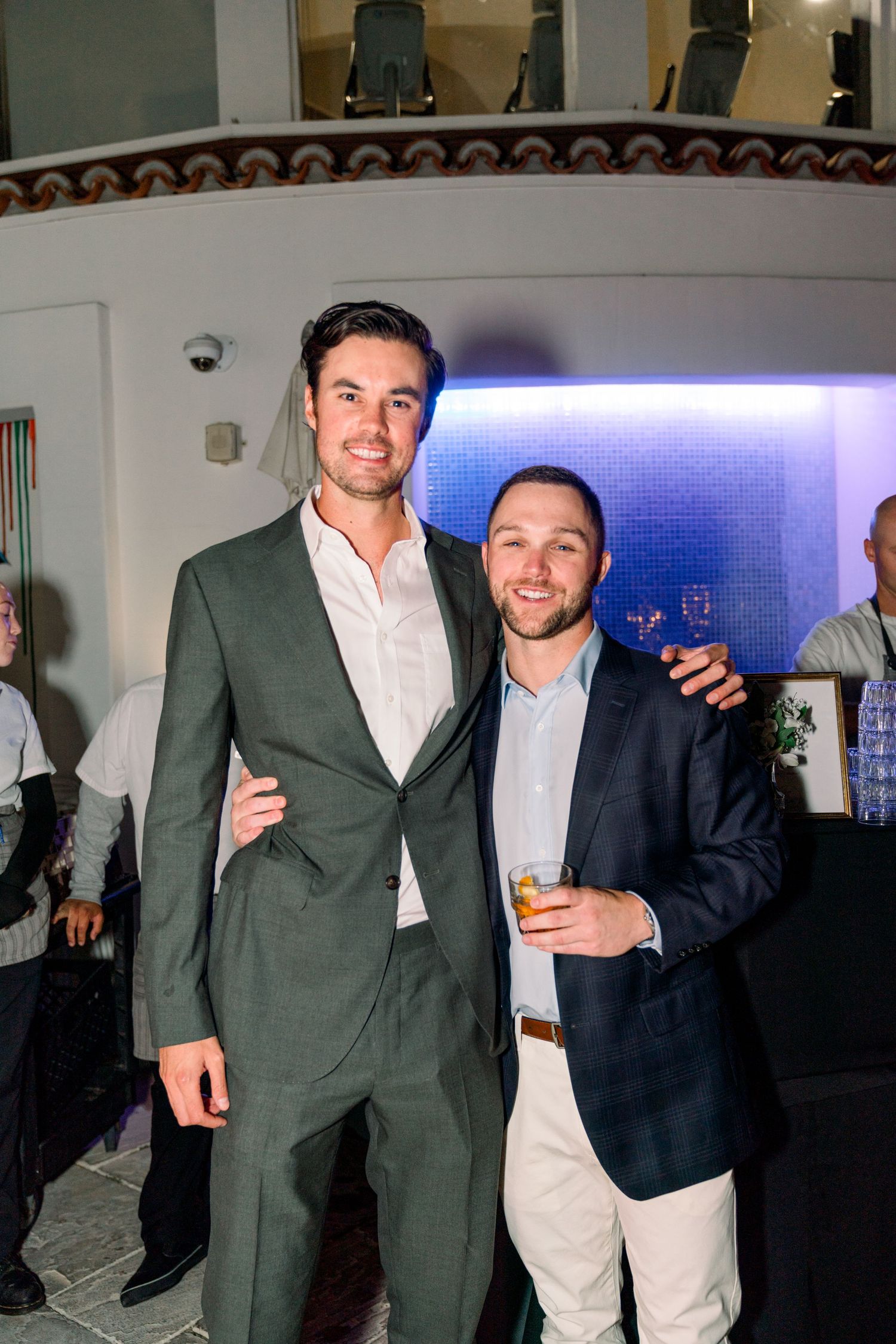 Two friends in suits enjoying drinks at an evening party indoors.