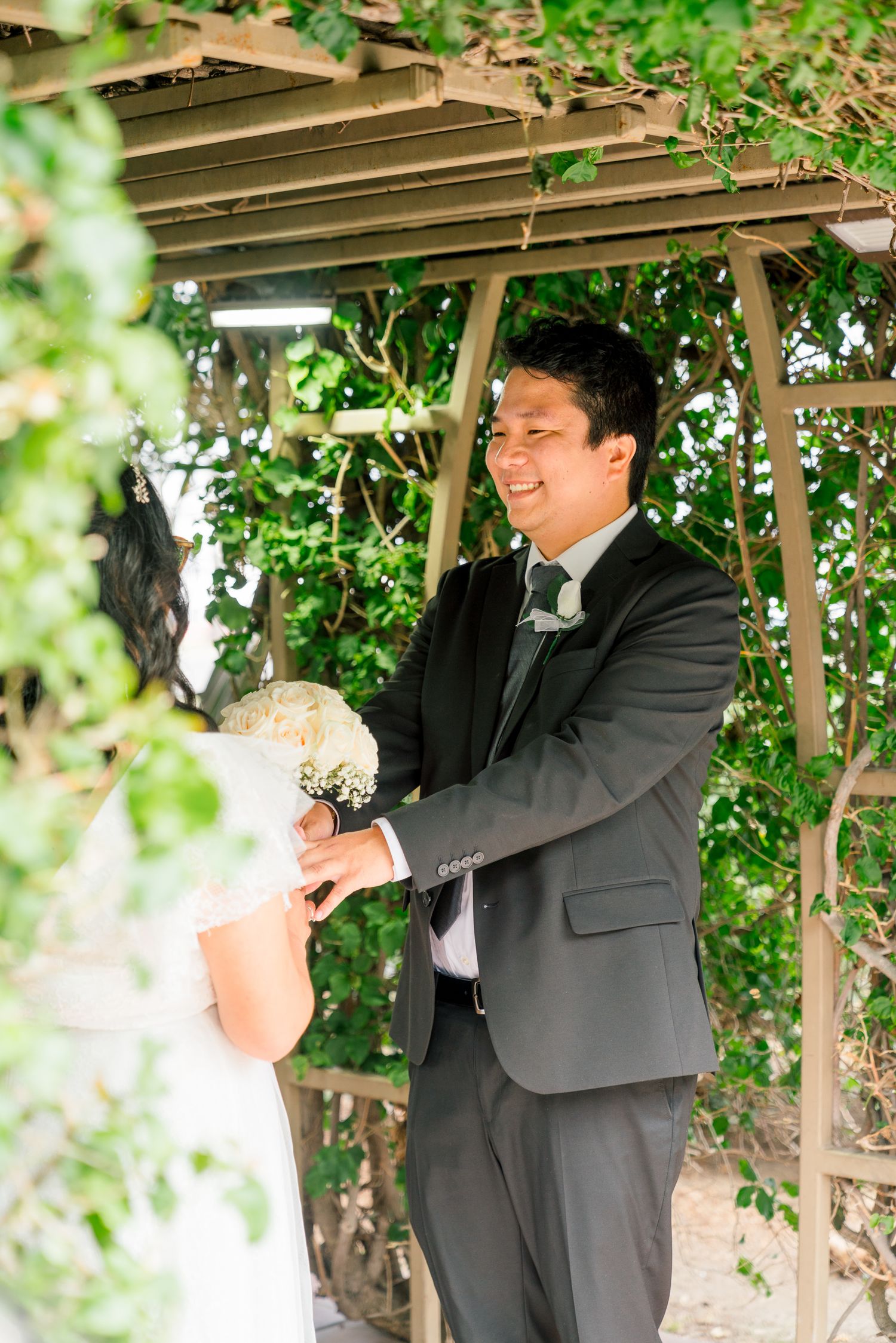 A joyful moment under a garden arbor covered in greenery during a wedding celebration.