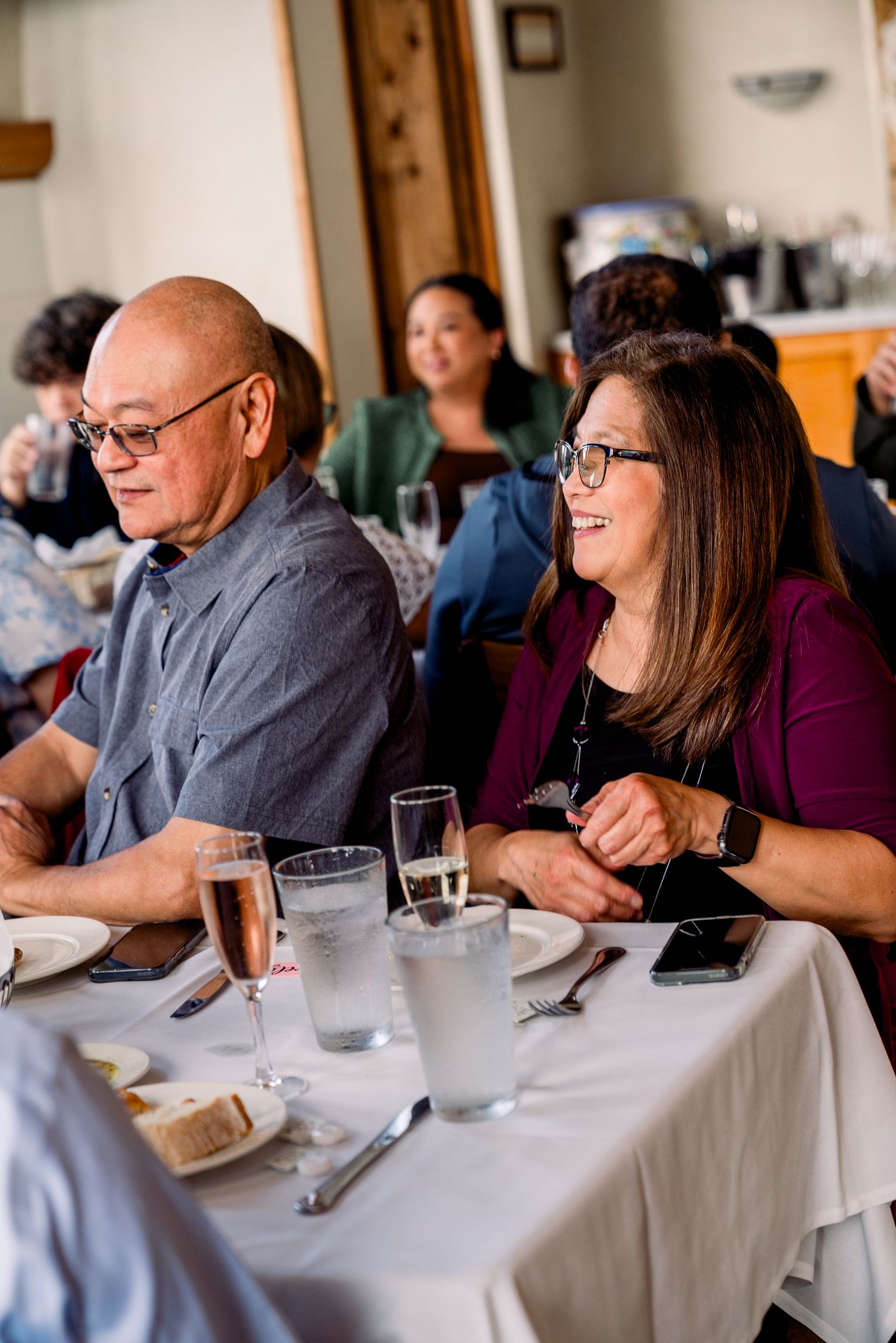 Wedding reception guests enjoying meal at tables with white linens in restaurant setting.