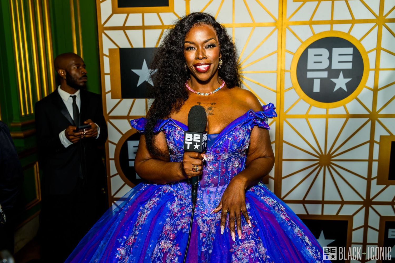 A person in a vibrant royal blue evening gown poses at an elegant event with gold decor in the background.