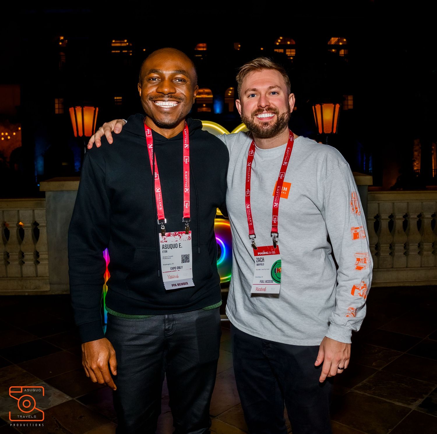 Two attendees posing together at evening event with decorative lights in background.