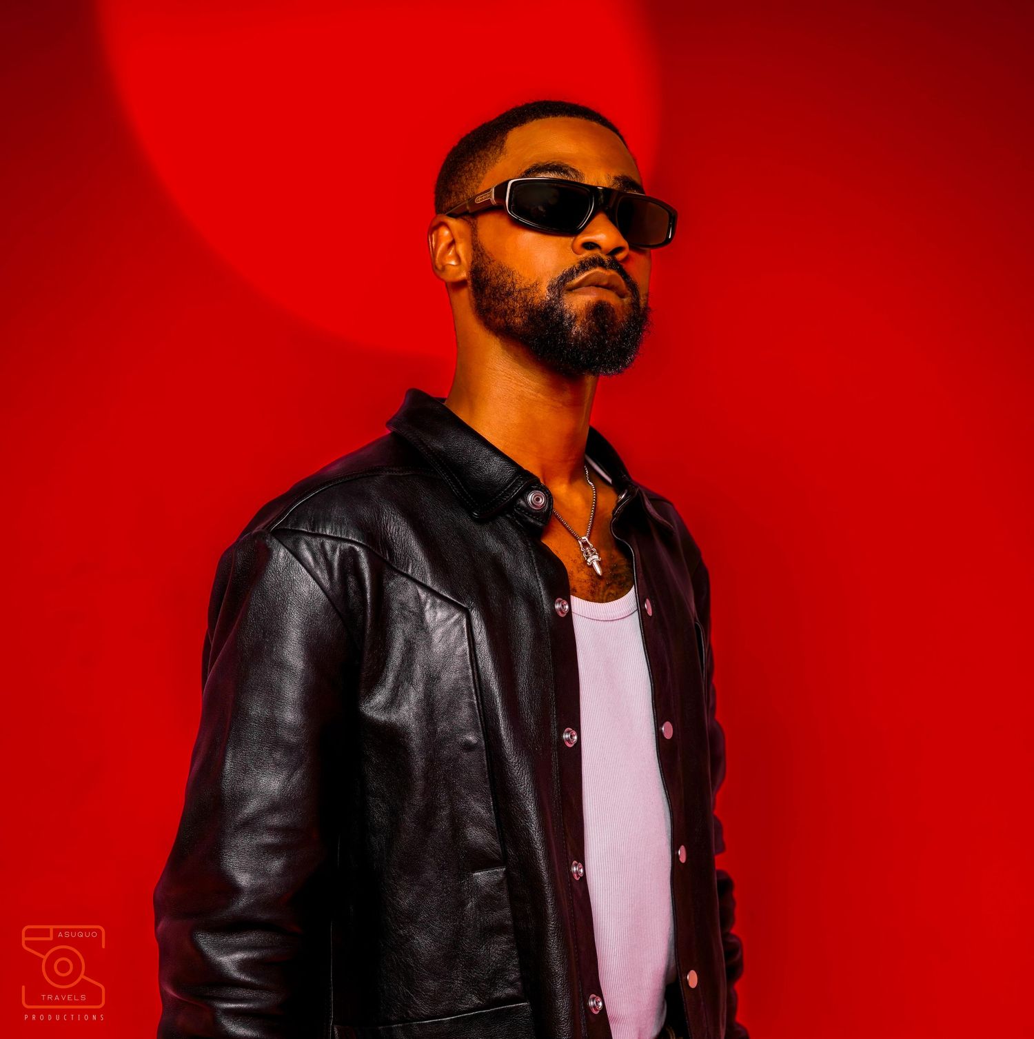 Stylish fashion portrait against vibrant red background showcasing leather jacket and sunglasses.