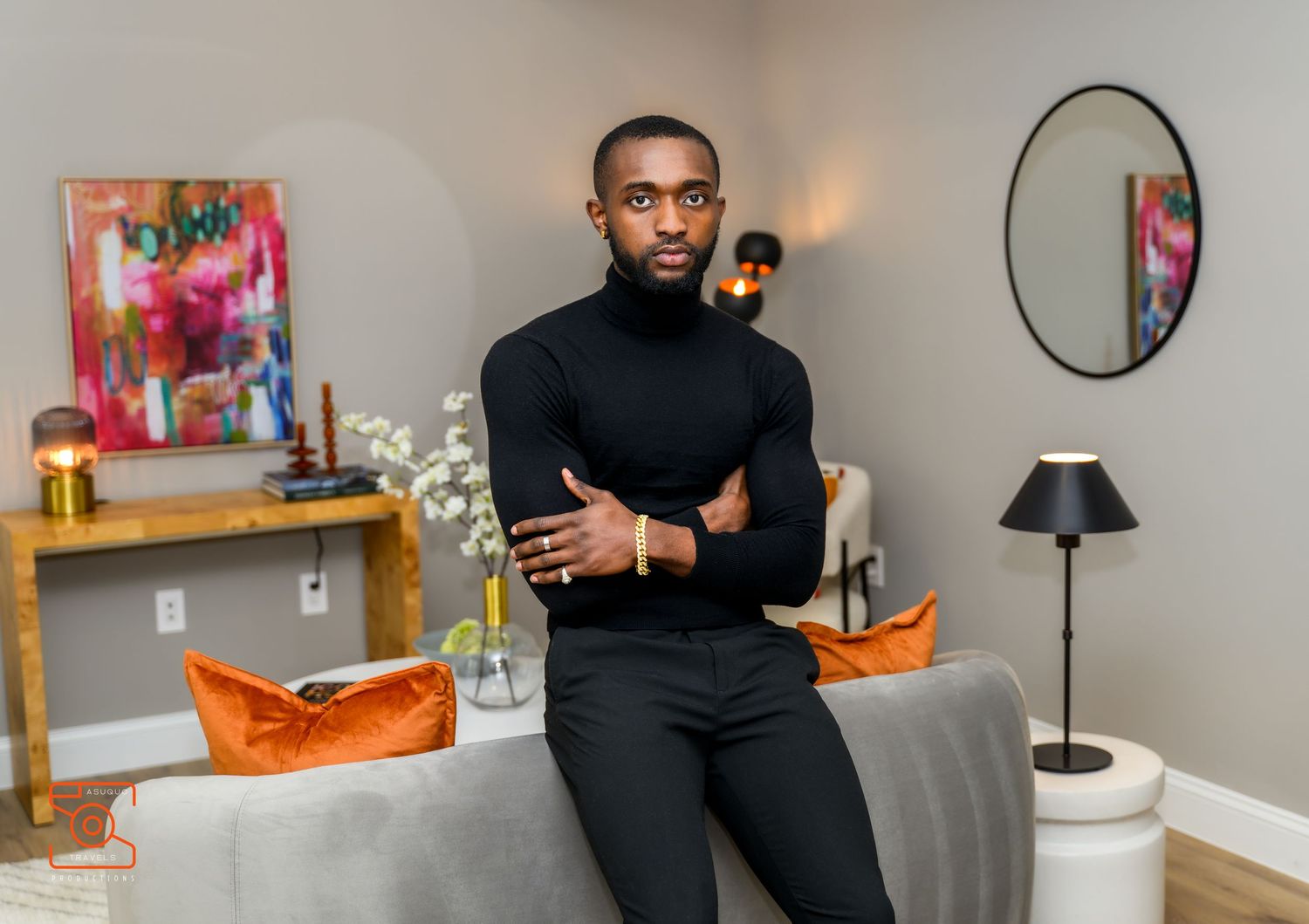 Person wearing black turtleneck sits in modern room with wooden shelves displaying colorful bottles and decor items.