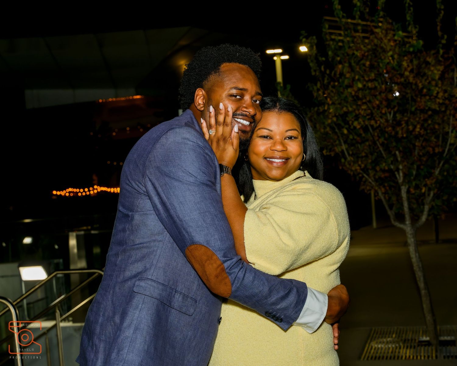 A joyful couple embracing and smiling outdoors at night, dressed in blue suit and yellow dress.