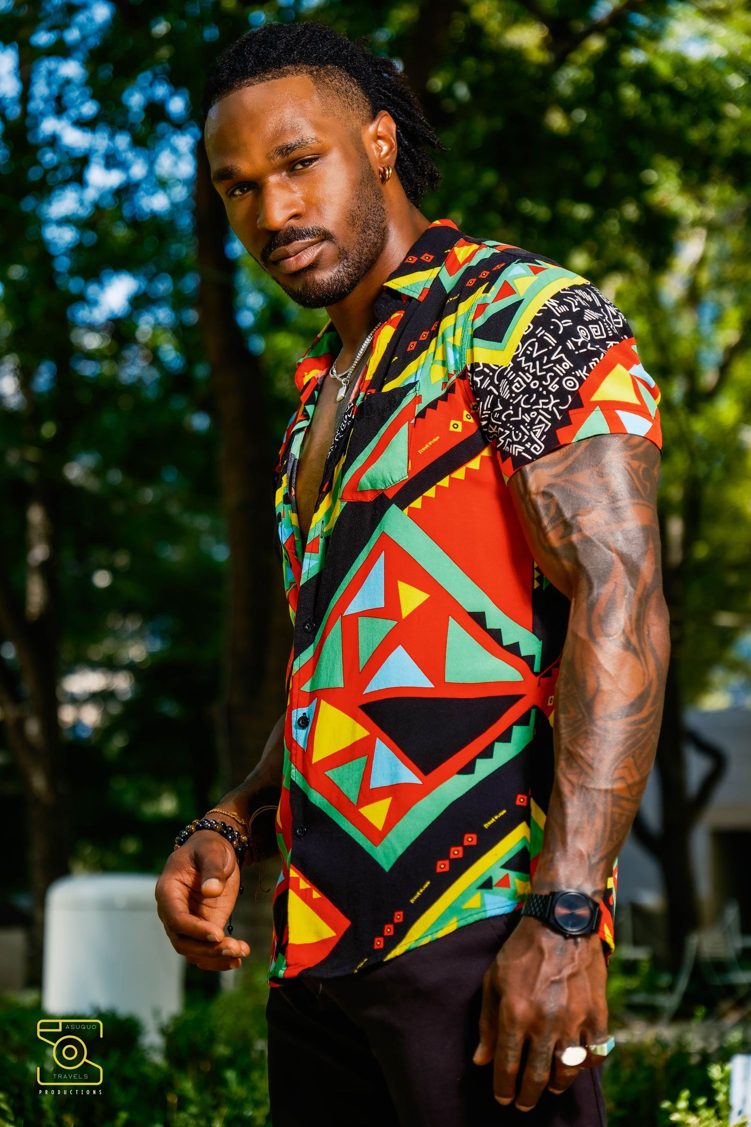 Modern African print sleeveless shirt featuring bold geometric patterns in red, yellow, and green against a black background.