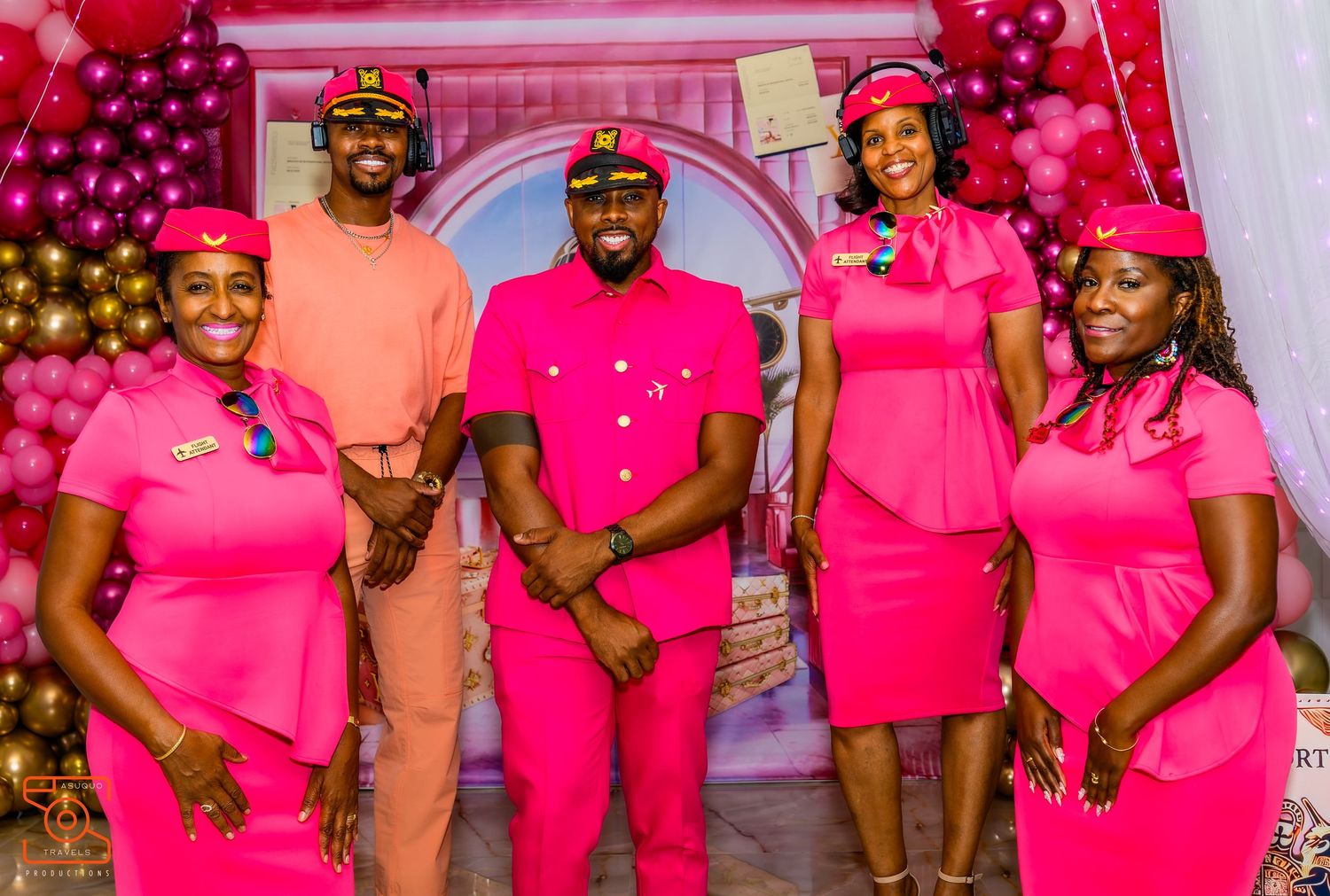 Group photo of wedding party members wearing coordinated bright pink outfits against festive backdrop.