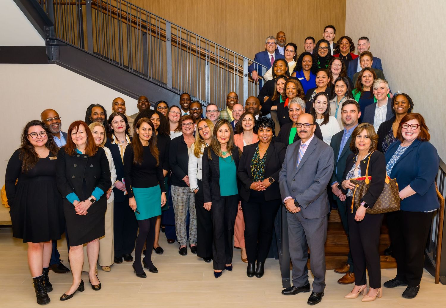 Large group photo of business professionals lined up in formal attire against a neutral background.