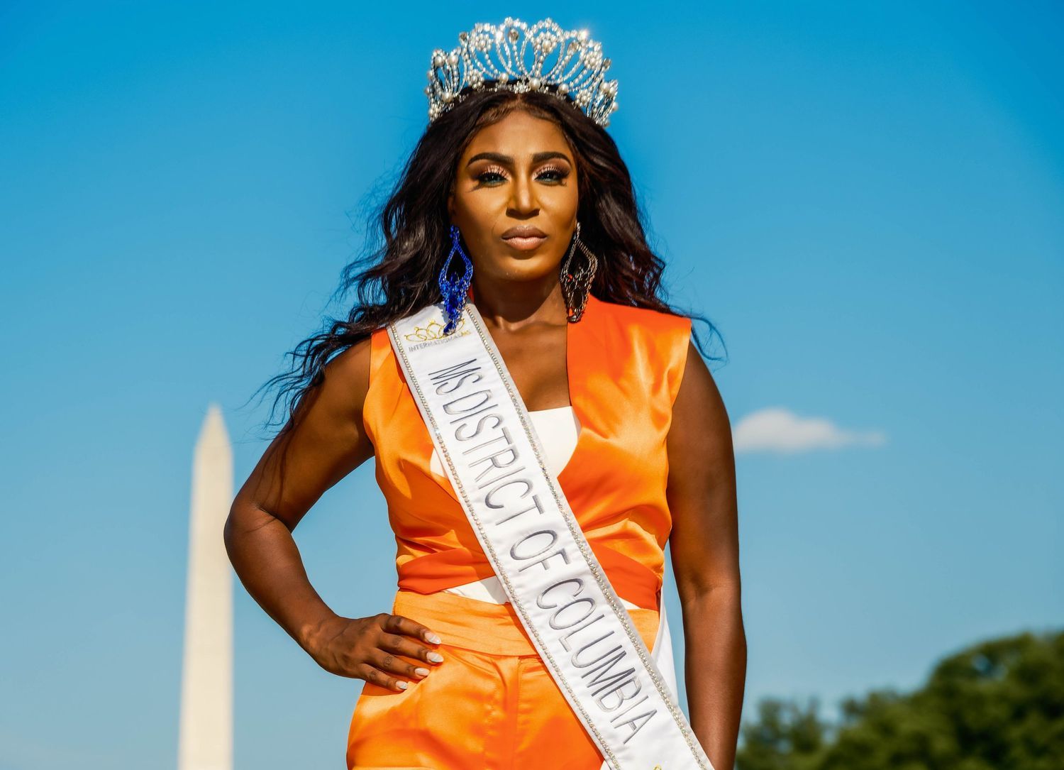 Women in orange sashes photographed outdoors against a bright blue sky.