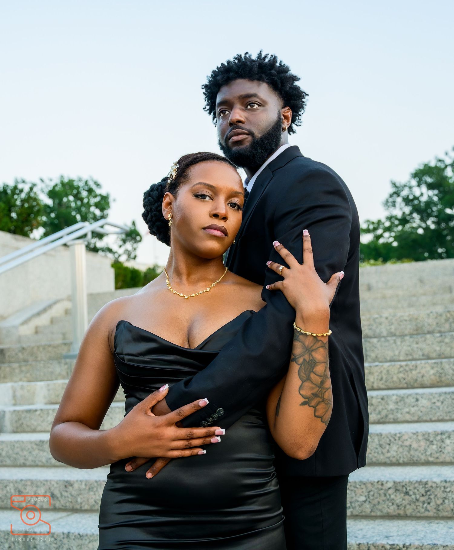 Elegant couple in matching black formal attire posing on outdoor steps for a stylish portrait photo.