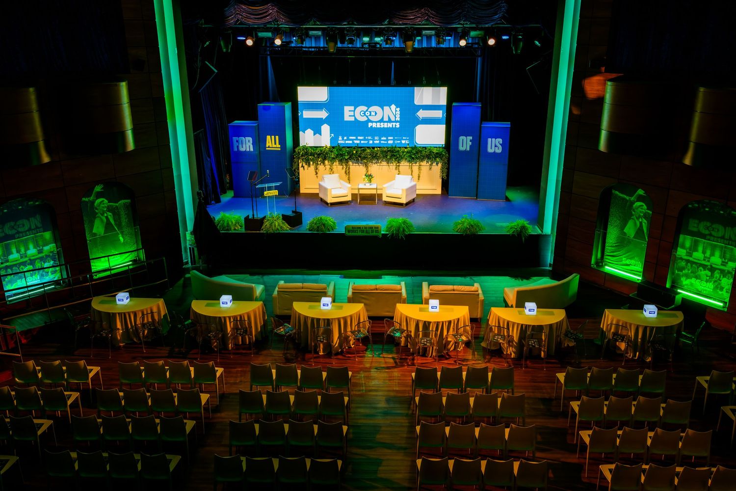 Large conference venue with green lighting and rows of empty seats facing a stage.