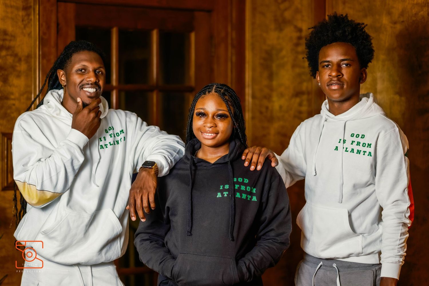 A group photo of people wearing white hoodies and dark clothing standing together in a warm-toned interior setting.