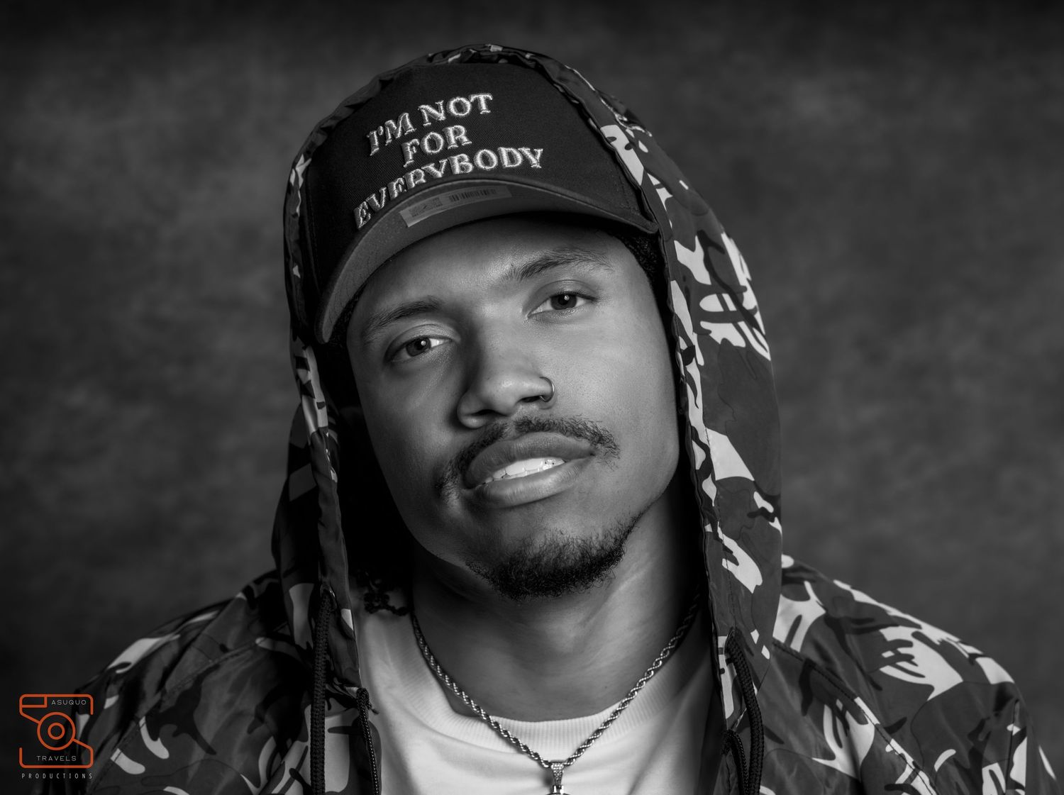 Black and white portrait of a man wearing a cap and hooded jacket, posing confidently for a professional photo.