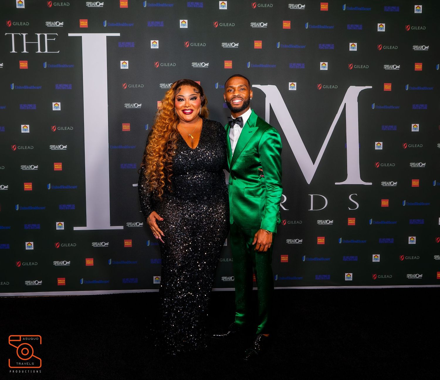 Two people pose at a formal event against a branded step-and-repeat backdrop featuring 'THE LM' lettering.