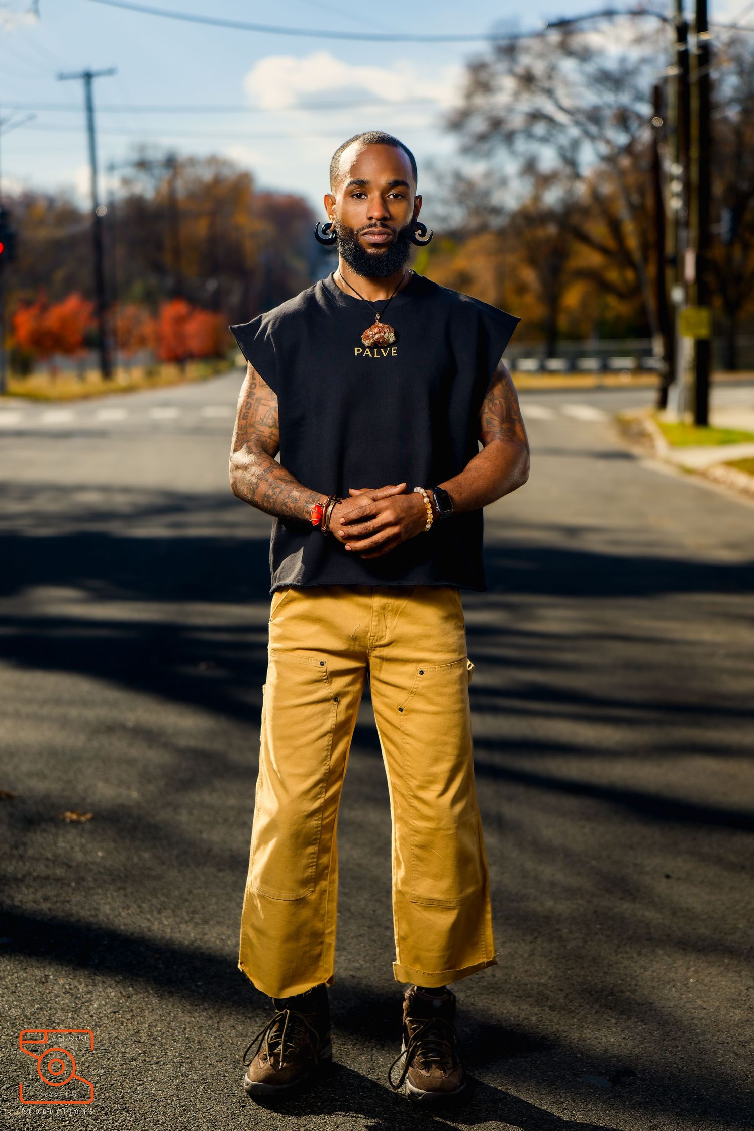 Professional outdoor fashion photography featuring khaki shorts and black top against an autumn street backdrop.