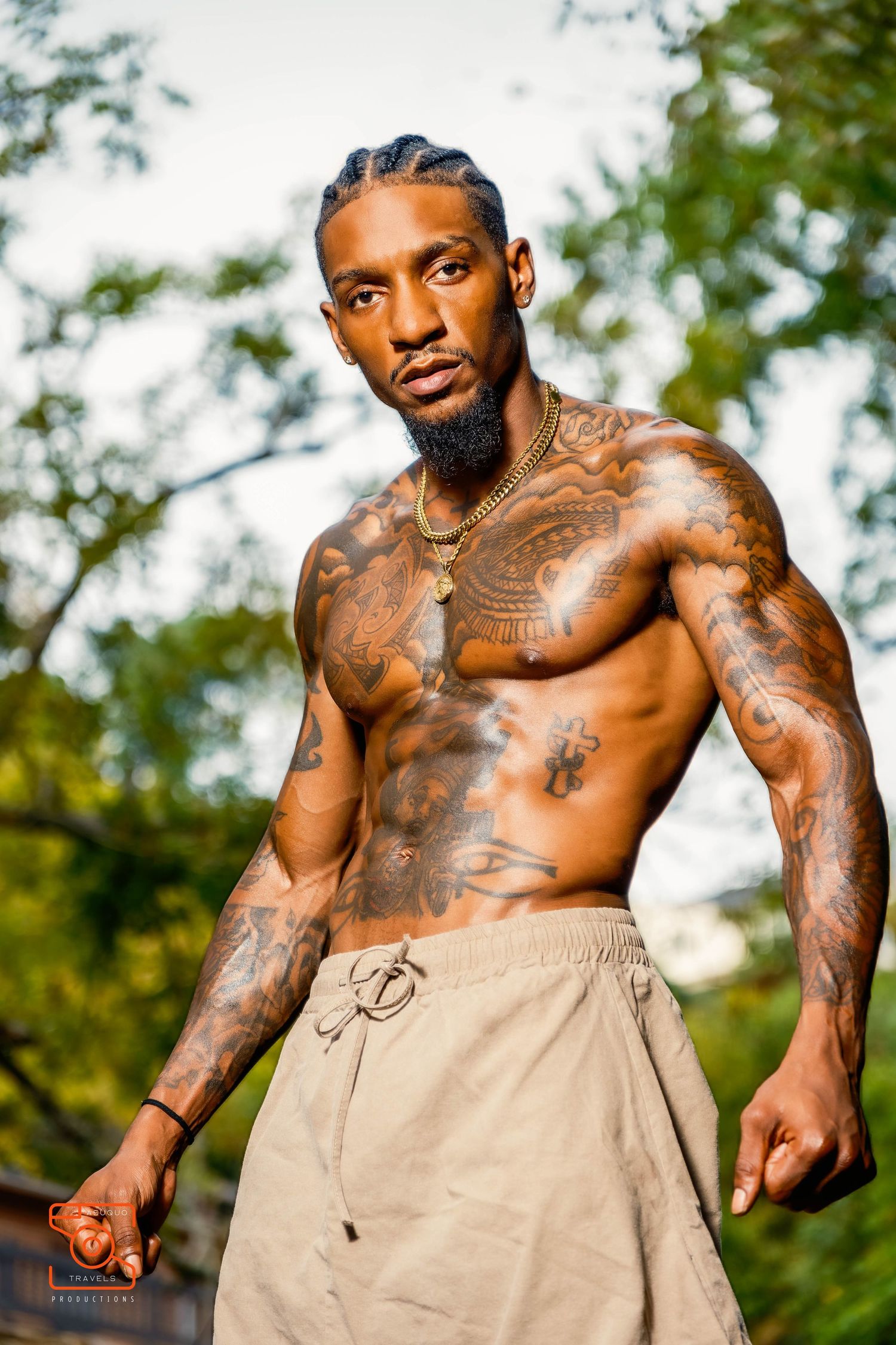 Athletic person with tattoos wearing light colored shorts poses outdoors in a nature setting during daytime.