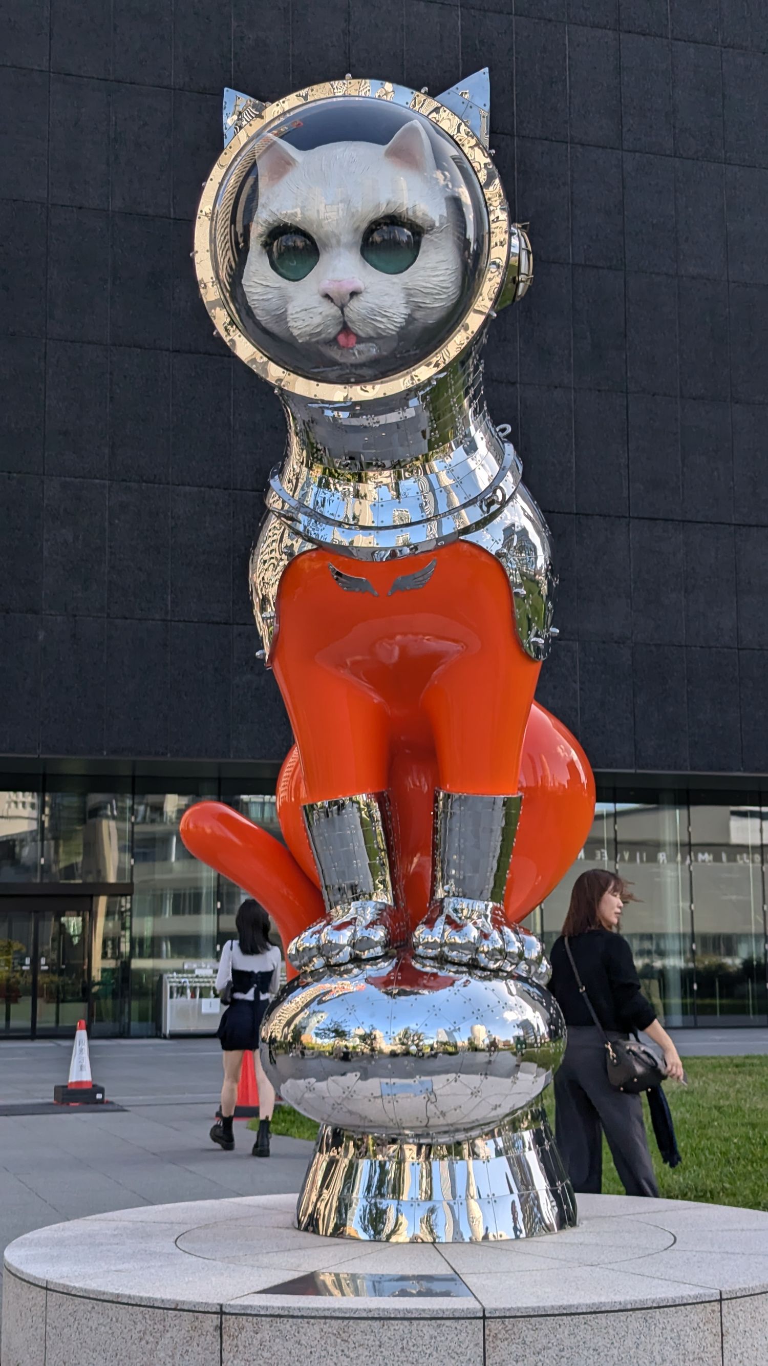 Large modern art sculpture of a cat in an astronaut suit and helmet displayed in an urban setting.