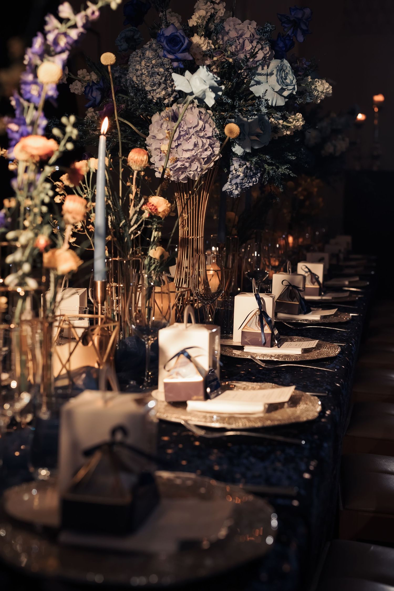 Elegant wedding table setting with dried flowers, glowing candlelight, and place settings on a dark tablecloth.