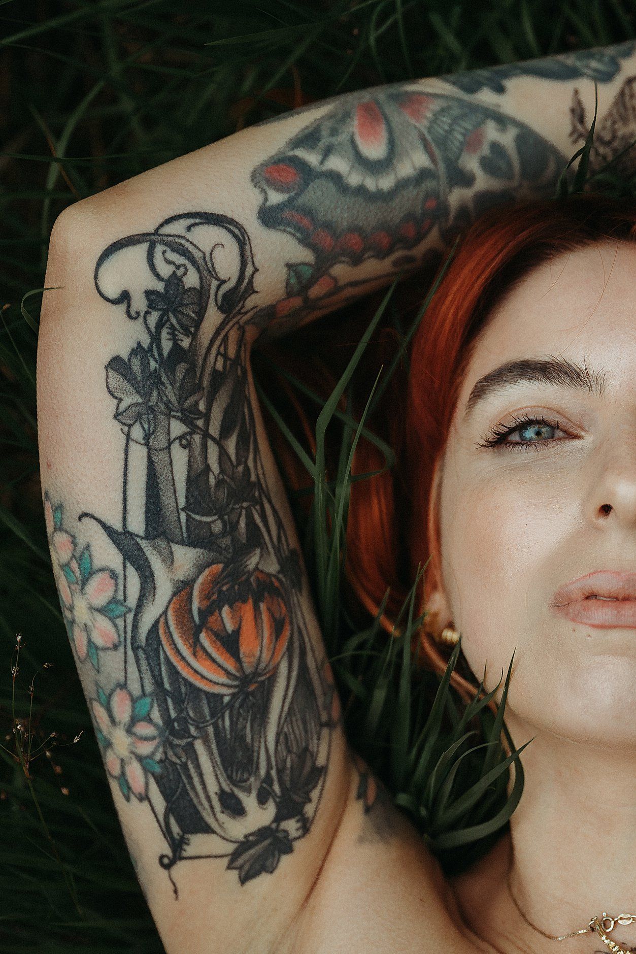 Frau mit Tattoo und rotem Haar liegt im Gras bei einem Fotoshooting in der Schweiz