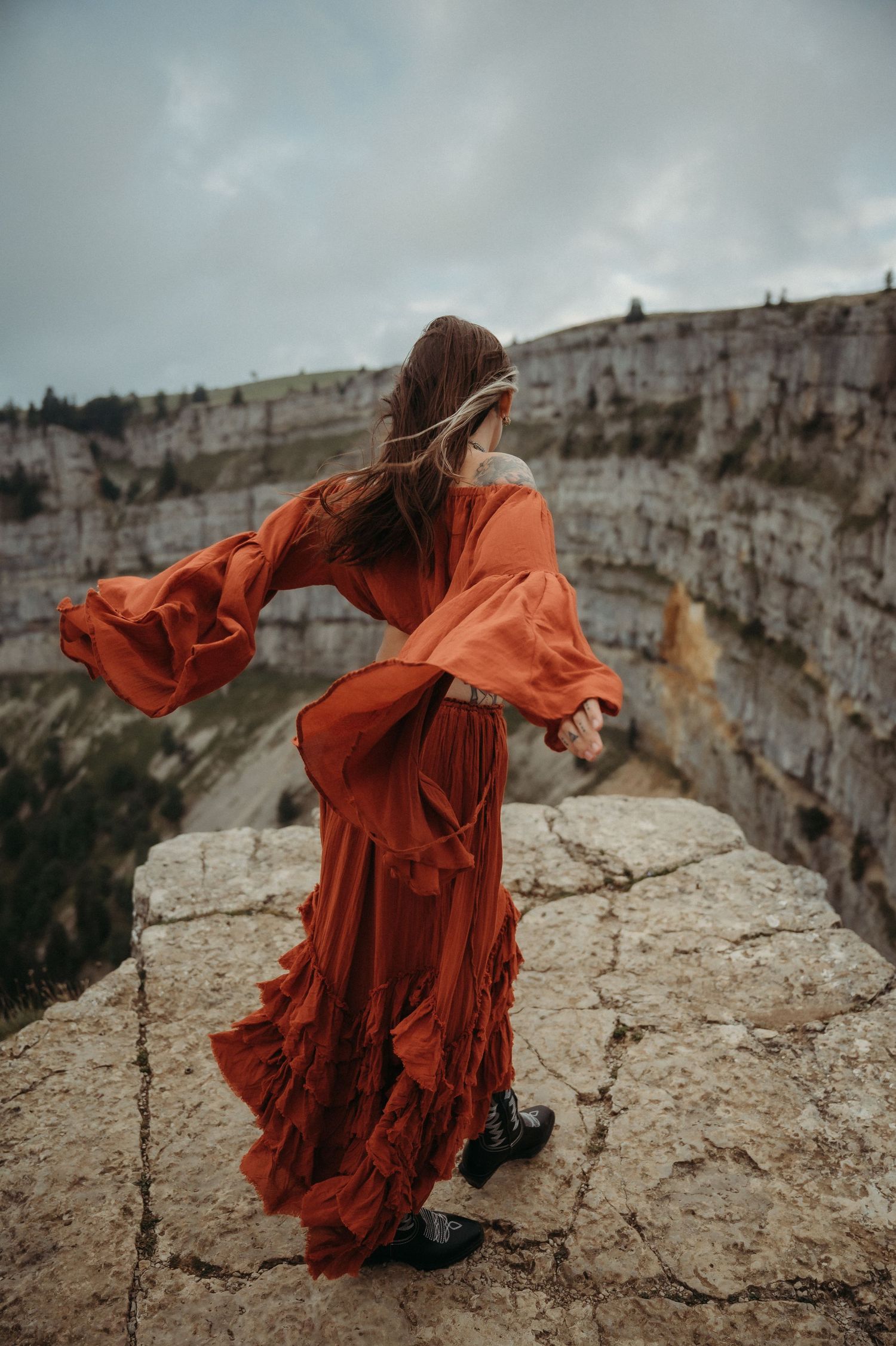 Frau in rotem Kleid am Creux du Van – kraftvolles Portrait vor dramatischer Felskulisse in der wilden Natur der Schweiz.