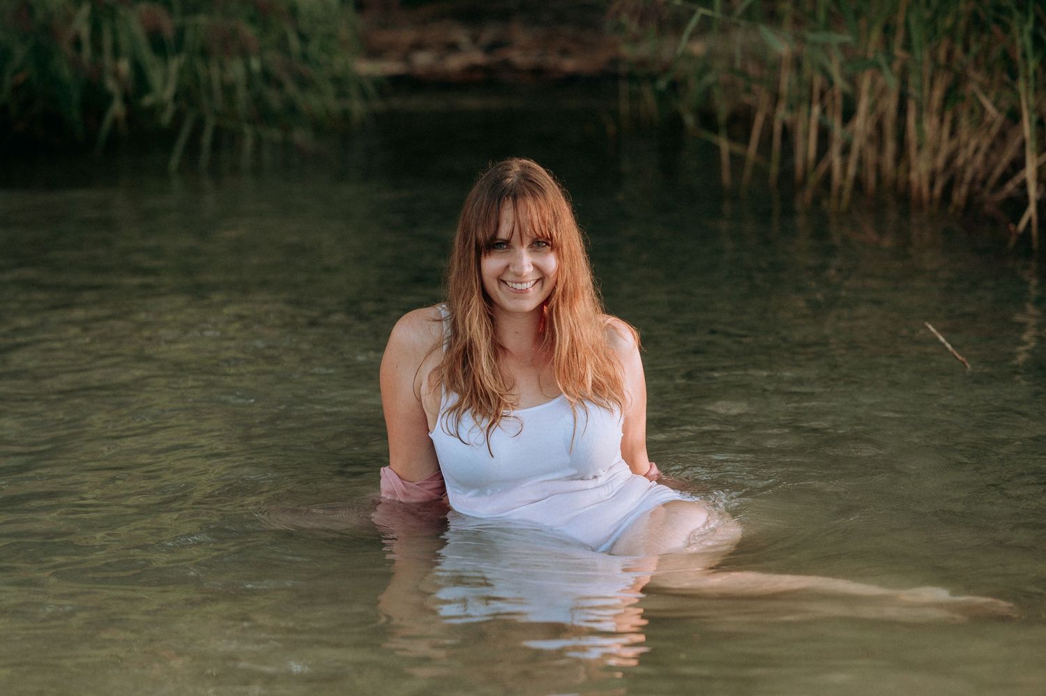 Boudoir-Shooting im Thunersee: Frau treibt in nassem Kleid im Wasser, Blick zur Kamera – sinnlich, ruhig, verwoben mit der Natur.