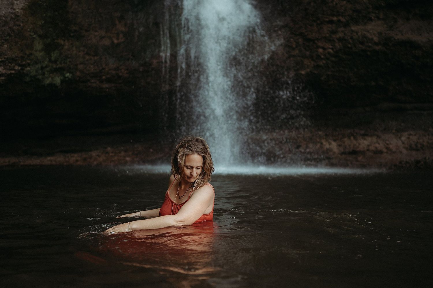 Frau in rotem Kleid steht im Wasser vor einem Wasserfall bei einem Fotoshooting im Berner Oberland