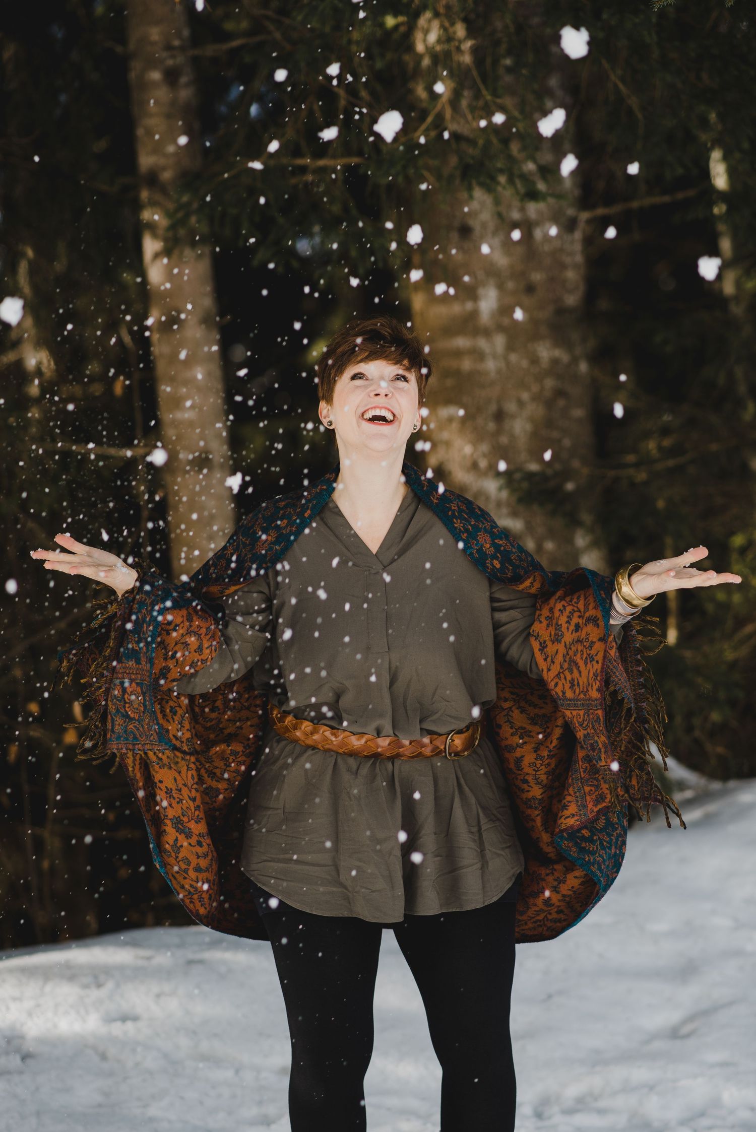 Fröhliche Frau wirft Schnee in die Luft, Winterporträt im Wald mit Boho-Outfit, natürliche Freude im Schnee bei Thun.