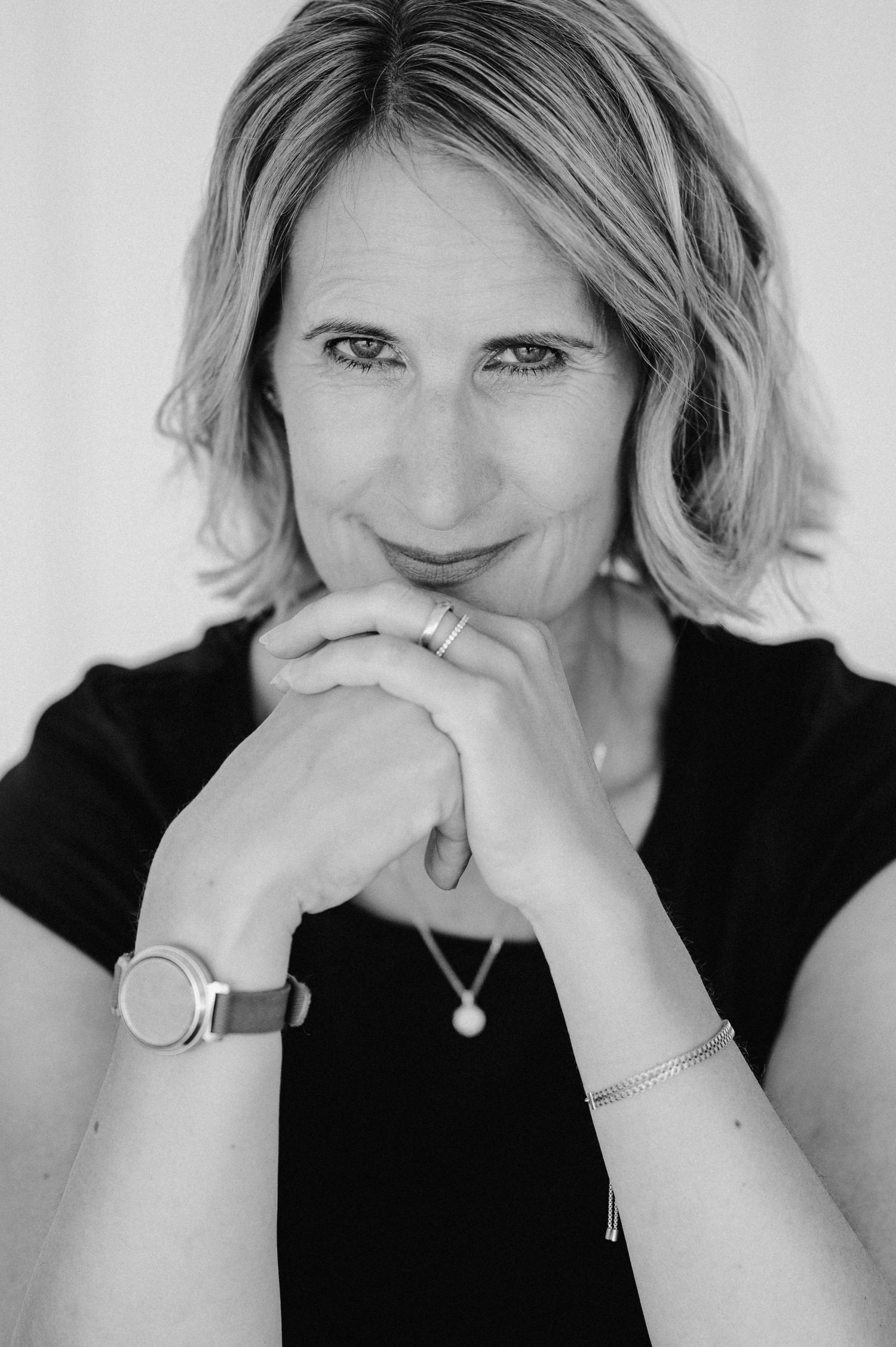 Schwarz-weiss Portrait einer Frau mit schulterlangem Haar, verschränkten Händen und direktem Blick, fotografiert in natürlichem Licht in Thu