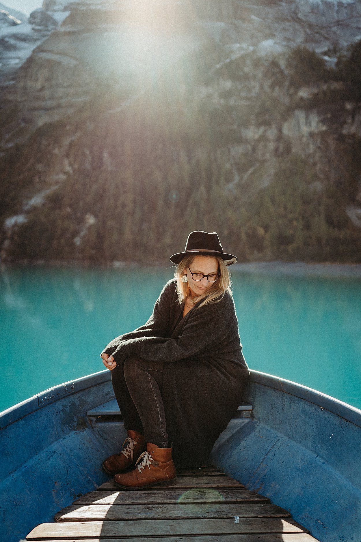 Person relaxes in blue canoe on stunning turquoise alpine lake surrounded by mountains during golden sunset.
