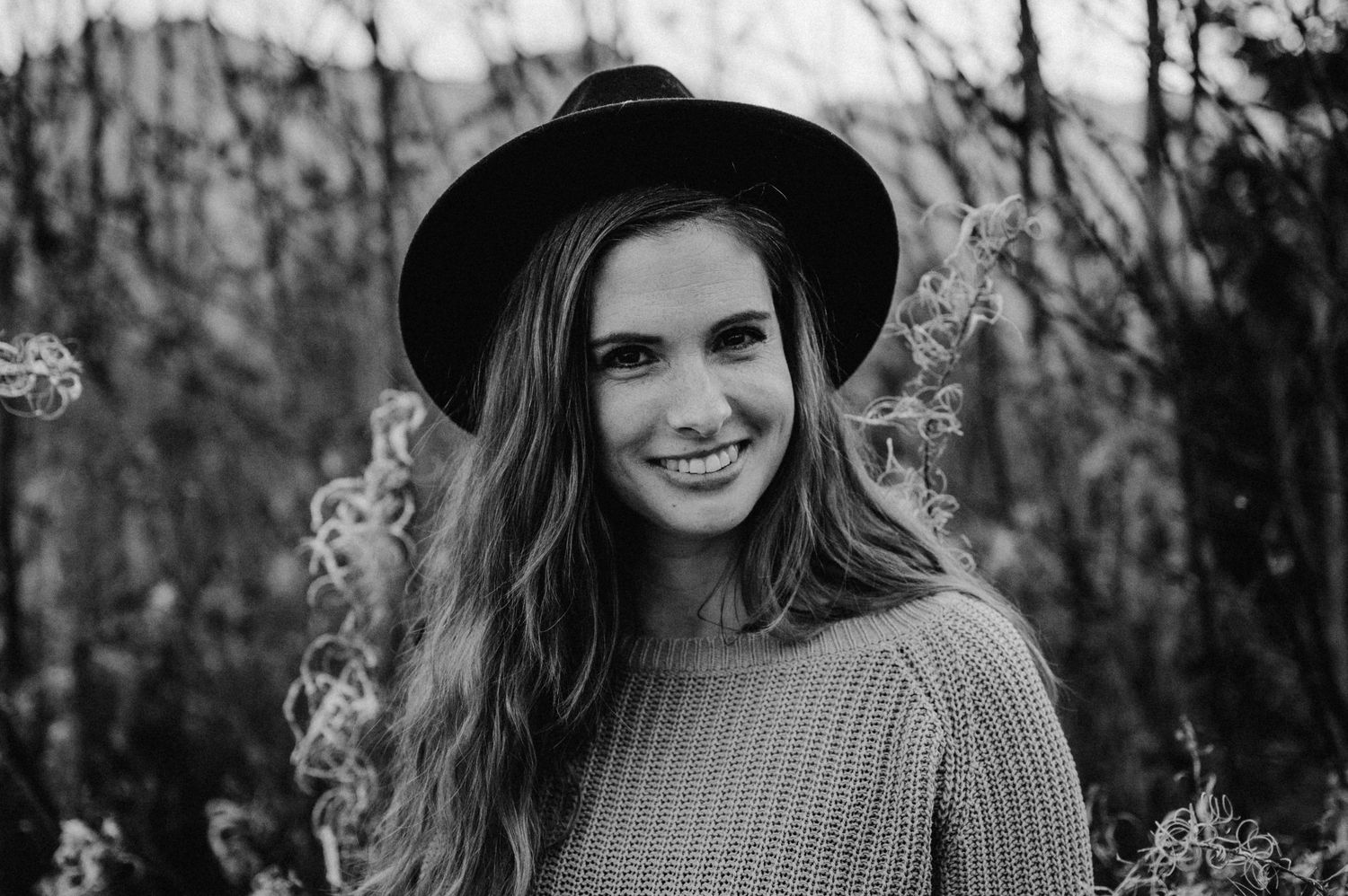 Porträt einer jungen Frau mit Hut und offenem Haar, aufgenommen in der Natur – ausdrucksstarkes Outdoor-Shooting in Schwarz-Weiss